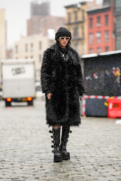 NEW YORK, NEW YORK - FEBRUARY 13: A model wears a black ribbed wool beanie, white sunglasses, a blac...