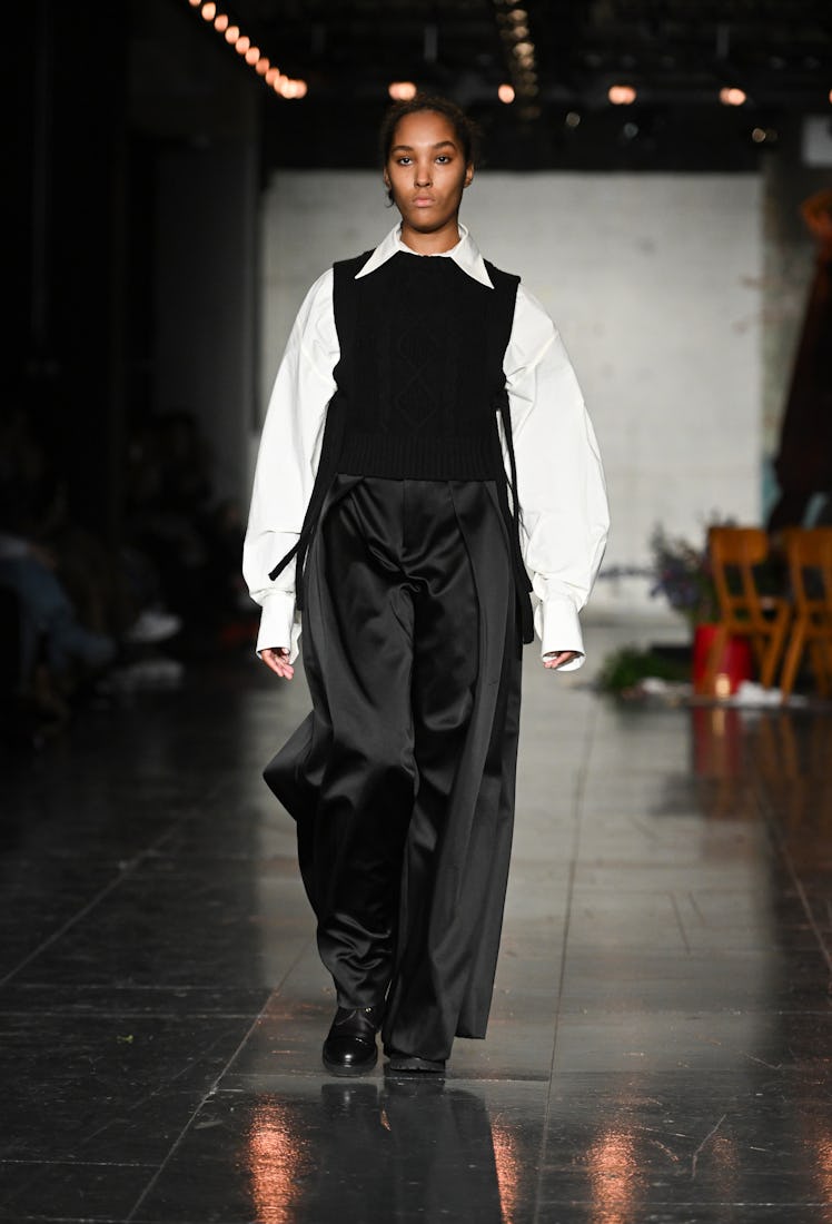 A model in a white shirt, black waistcoat and satin trousers by S. S. Daley at the London Fashion We...