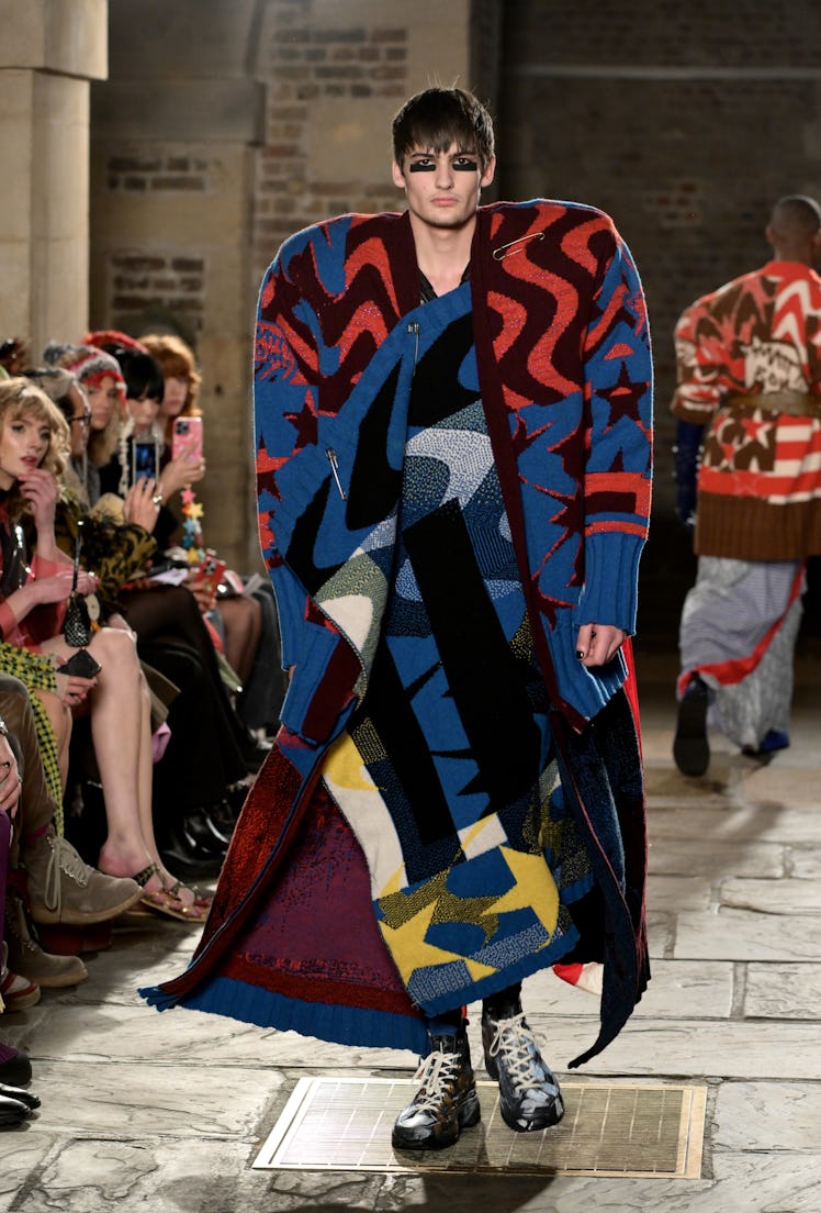 A model wearing a multi-colored oversized asymmetric knit outfit by Matty Bovan