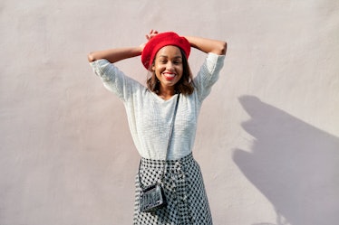 young woman wearing a red bedet smiles at camera as she thinks about full moon in leo (aka the Febru...