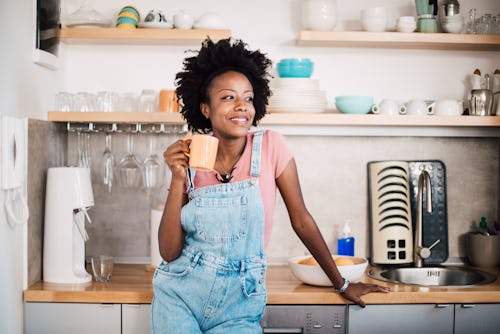 A woman wearing overalls enjoys coffee at home. Here's your daily horoscope for February 3 2022