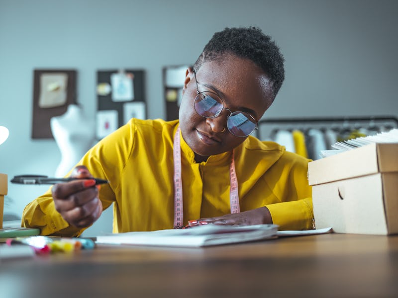 Focused african girl student study online at home making notes in notebook sit at home office desk, ...