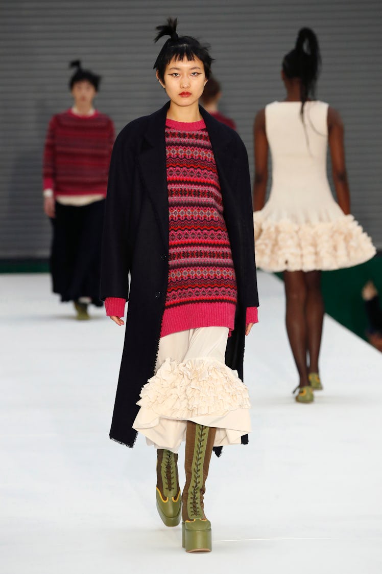 A model in a red sweater, black cardigan and beige skirt by Molly Goddard at the London Fashion Week...