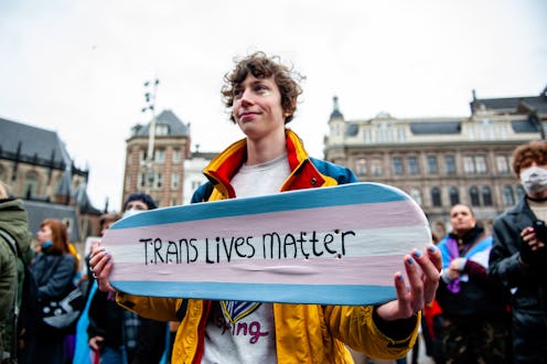 A person is holding a skateboard with the colors of the transgender flag and with a message in suppo...