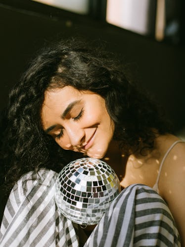 Young woman holding a disco ball and smiling, thinking about the February 28, 2022 weekly horoscope ...