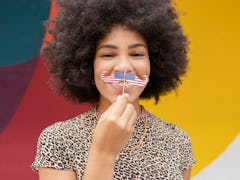 young woman holds american flag mustache up to her face and smiles, as she discusses the pluto retur...