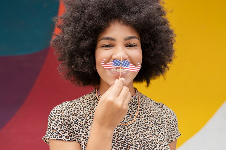 young woman holds american flag mustache up to her face and smiles, as she discusses the pluto retur...