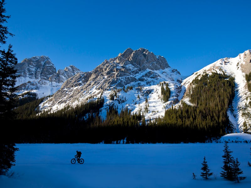 A man goes for a winter fat bike ride along the edge of a frozen lake in the Rocky Mountains of Cana...