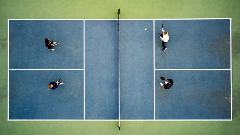 A group of young adults playing Pickleball on an outdoor court.
