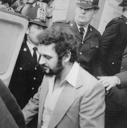 Yorkshire Ripper, Peter Sutcliffe, (with beard), is shown leaving court under heavy police guard aft...