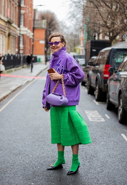 LONDON, ENGLAND - FEBRUARY 20: A guest is seen wearing purple jacket, bag, green skirt, green socks,...