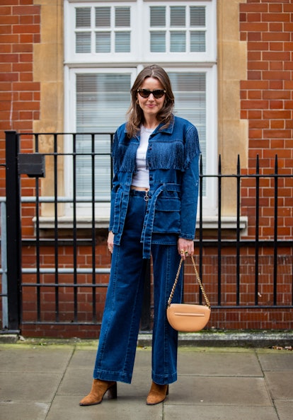 LONDON, ENGLAND - FEBRUARY 20: A guest is seen wearing denim jacket, jeans, Burberry bag in beige, s...