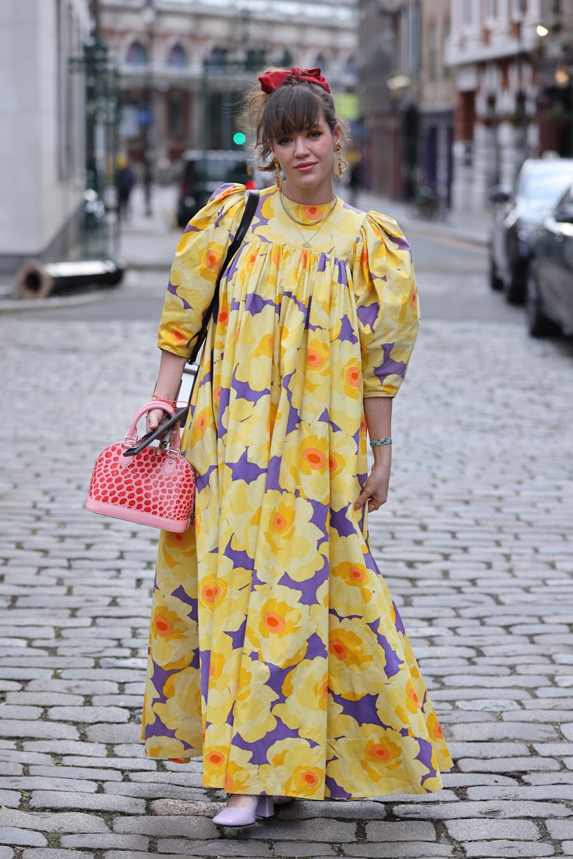 LONDON, ENGLAND - FEBRUARY 21: A guest wearing long floral print dress, red patterned handbag, red h...