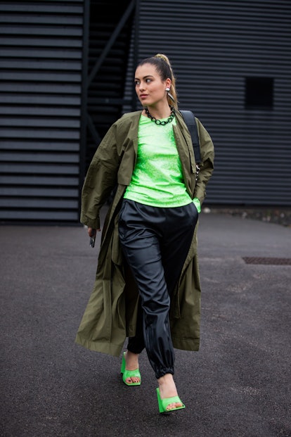 LONDON, ENGLAND - FEBRUARY 20: A guest is seen wearing neon top, black pants, olive trench coat, neo...