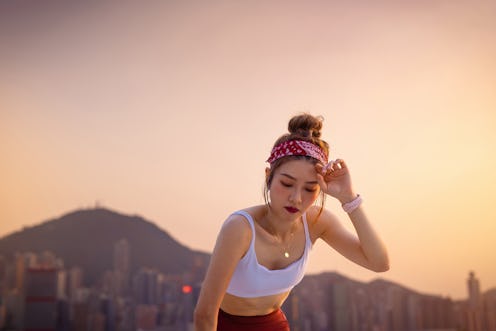 Exhausted young Asian sports woman taking breath after working out outdoors in the city at sunset, l...