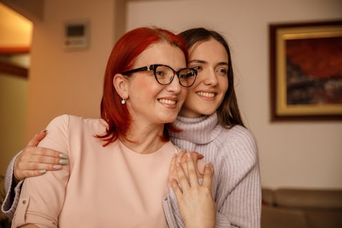 Portrait of happy young woman embracing her loving mother. They are both looking away, smiling and c...