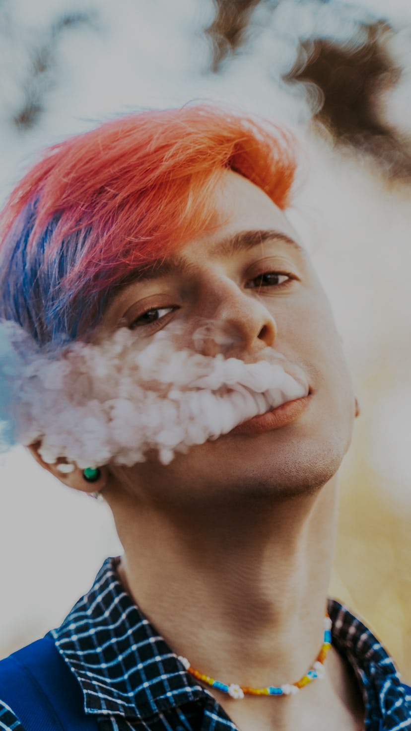 Young hipster with purple, very peri colored hair and piercing is smoking vape or electronic cigaret...