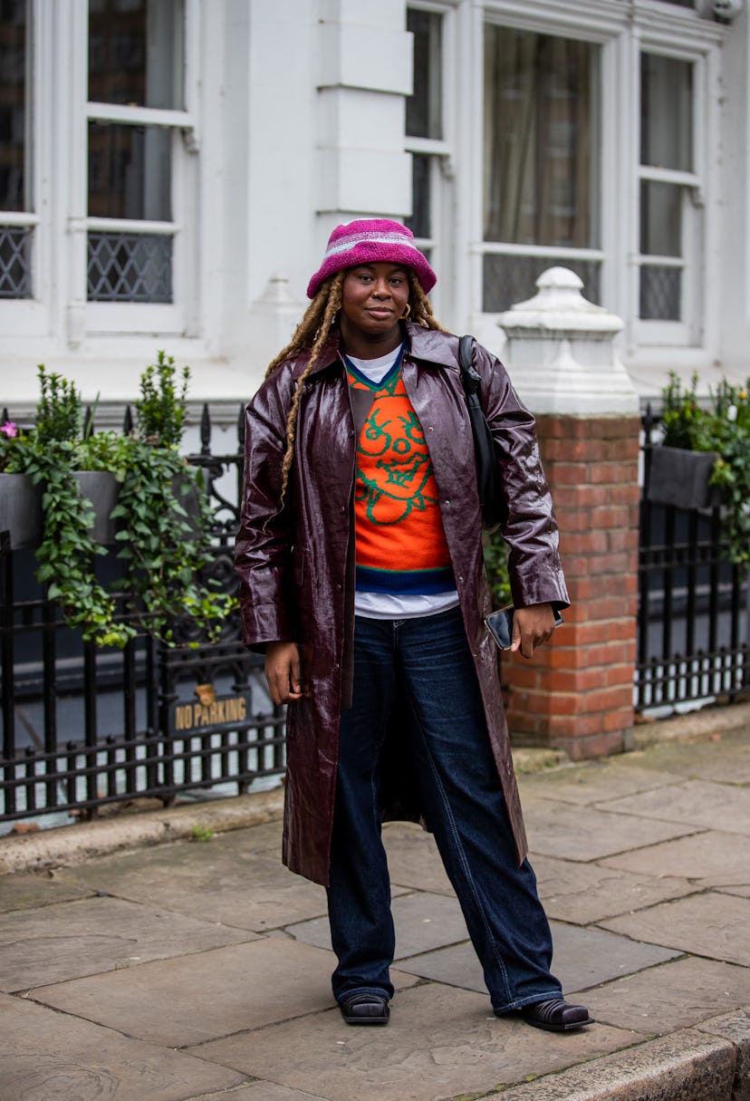 LONDON, ENGLAND - FEBRUARY 19: A guest is seen wearing bucket hat, bordeaux colored vinyl coat, dark...