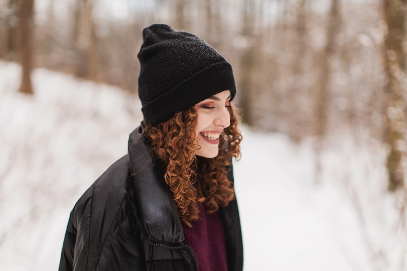 Redhead curly beautiful girl in jacket and hat in forest. Portrait with smile. Winter break. Woman e...