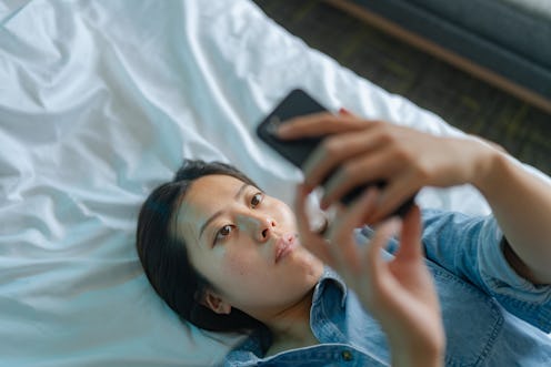 A high angle view of a young woman using a smart phone while lying down. Think your Instagram accoun...
