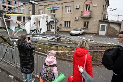 People are seen outside the cordoned off area around the remains of a shell in a street in Kyiv on F...