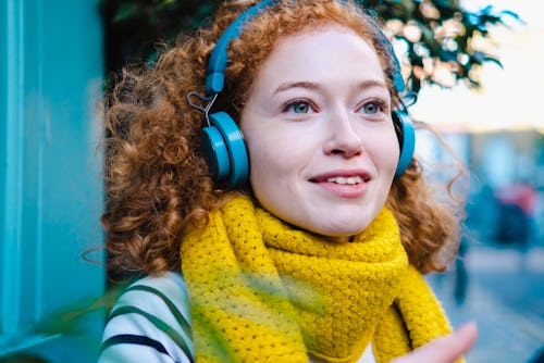portrait close-up of a woman wearing a yellow scarf and headphones smiling and looking into the dist...