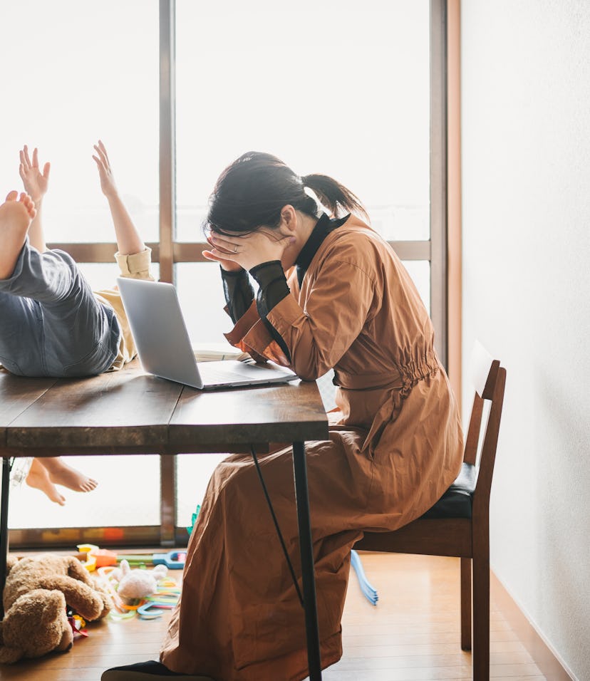 Asian mother working with laptop while her son and daughter are playing in the living room. Her son ...