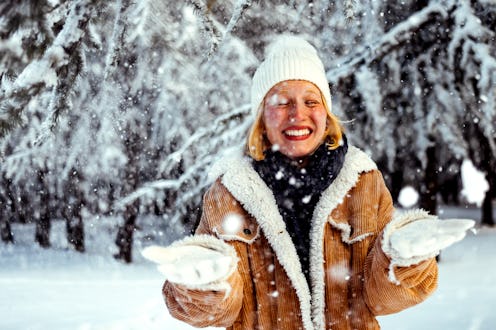A beautiful young girl in a knitted hat throws snow in the winter forest