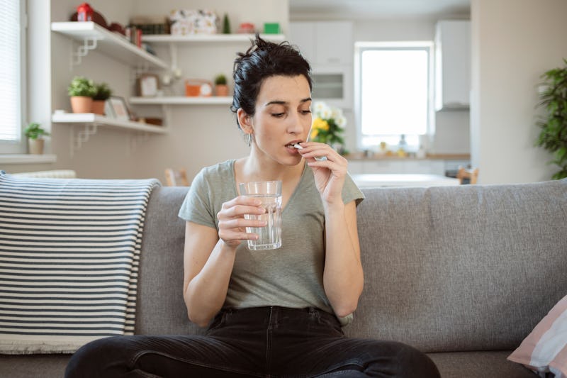 Beautiful young woman taking pill at home