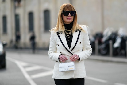 MILAN, ITALY - FEBRUARY 24: A guest wears black futurist sunglasses, gold chain necklaces, a white t...