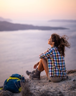 Young female backpacker taking a break after hiking on a hill above the sea at sunset. Here's your M...