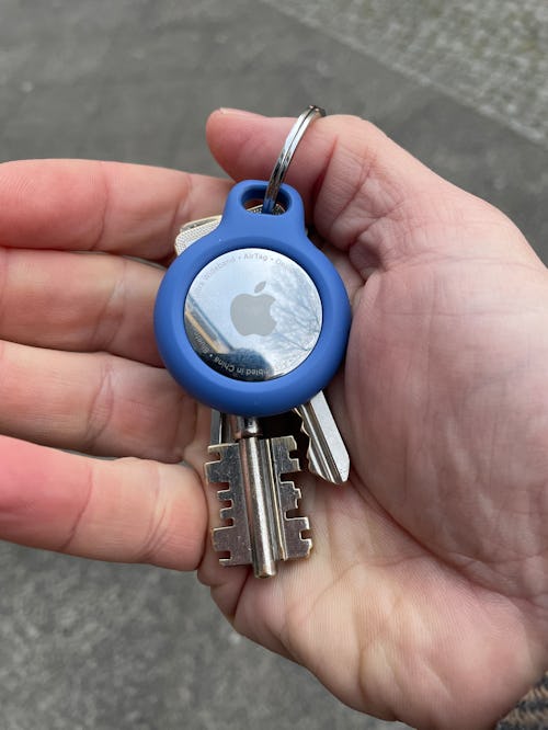 A hand is holding a set of keys with an Apple AirTag attached to the key ring. Here's how airtags wo...