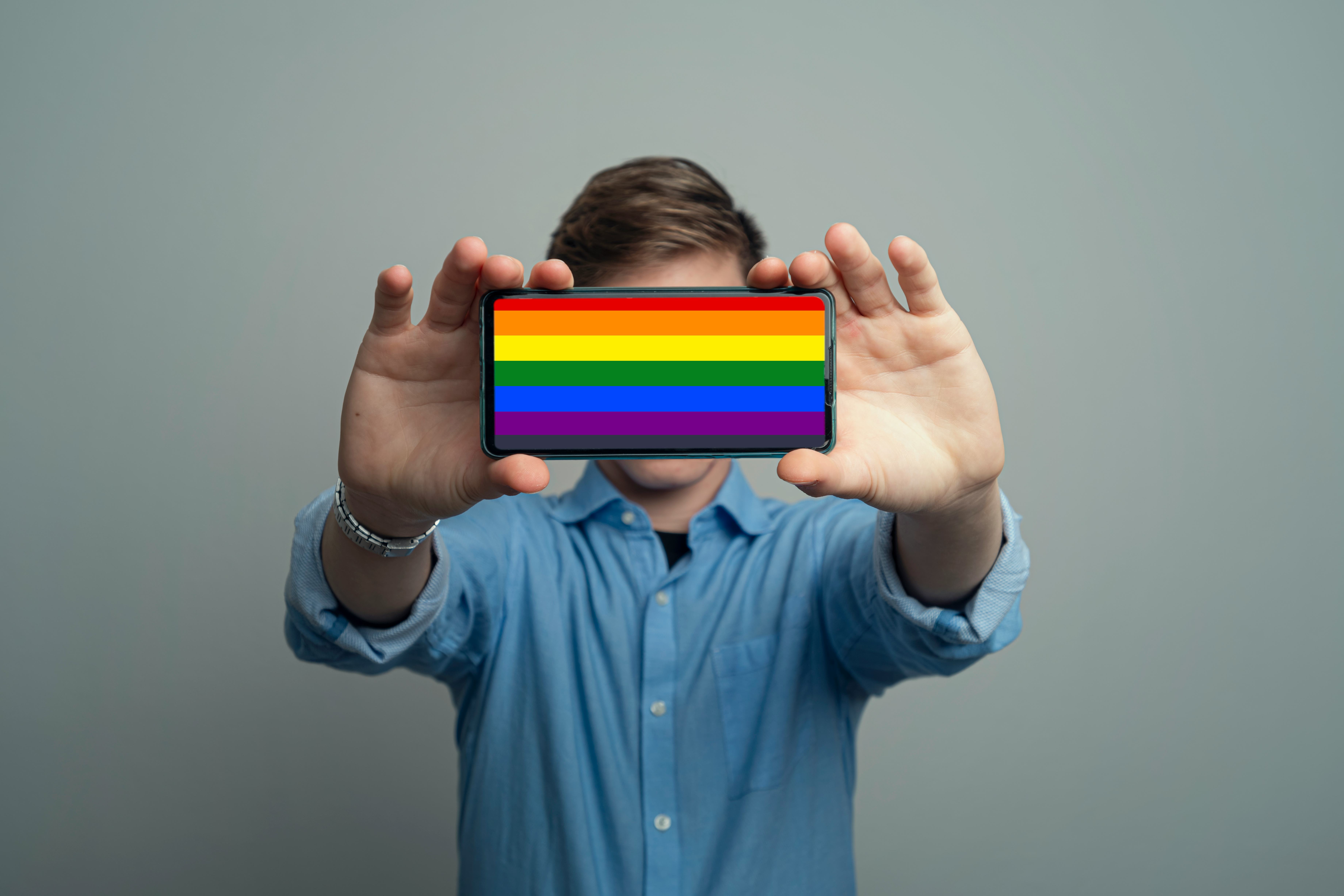 oung man Holding Smartphone With a Rainbow or Pride Flag
