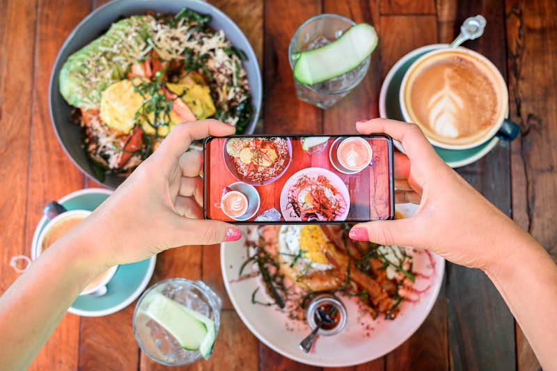 A woman takes a photo of a brunch spread. Can you eat in the metaverse? Experts explain what food wi...