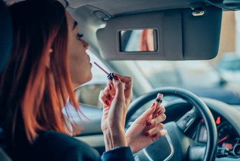 Young business woman putting a lip gloss in the front seat of a car
