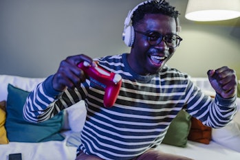 A young African-American man is at home on the couch, he is having fun playing video games