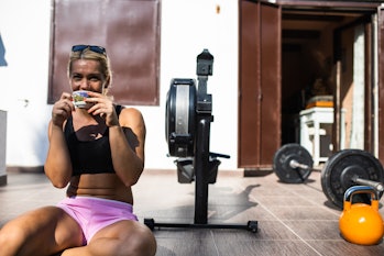 A fit young woman is having coffee before working out on a rowing machine on her patio on a sunny da...