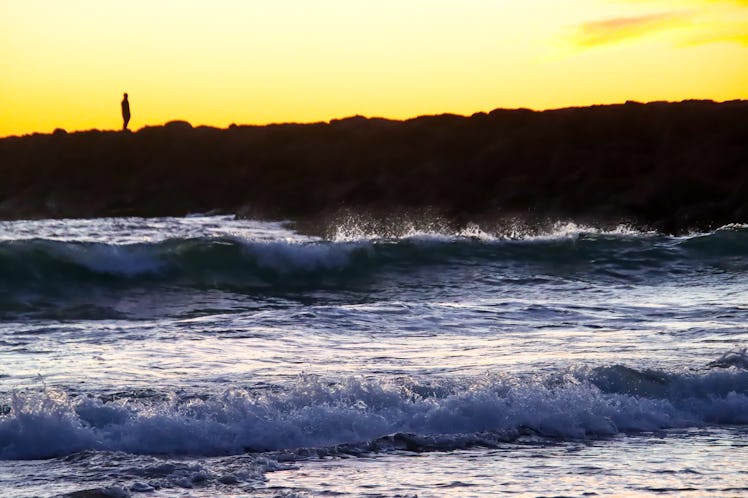 A lone man on a jetty is silhouetted at sunset at Silver Strand Beach in Oxnard, California. Image c...