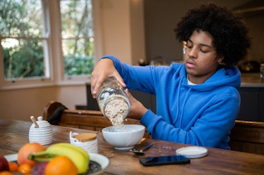 Teenage boy sitting at the kitchen table pouring meusli into his breakfast bowl