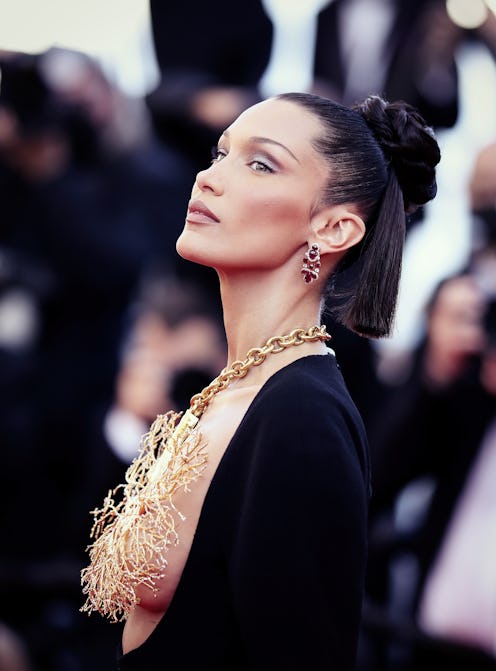 Bella Hadid wearing a black dress and a golden tree shaped necklace that covers her breast, with the...
