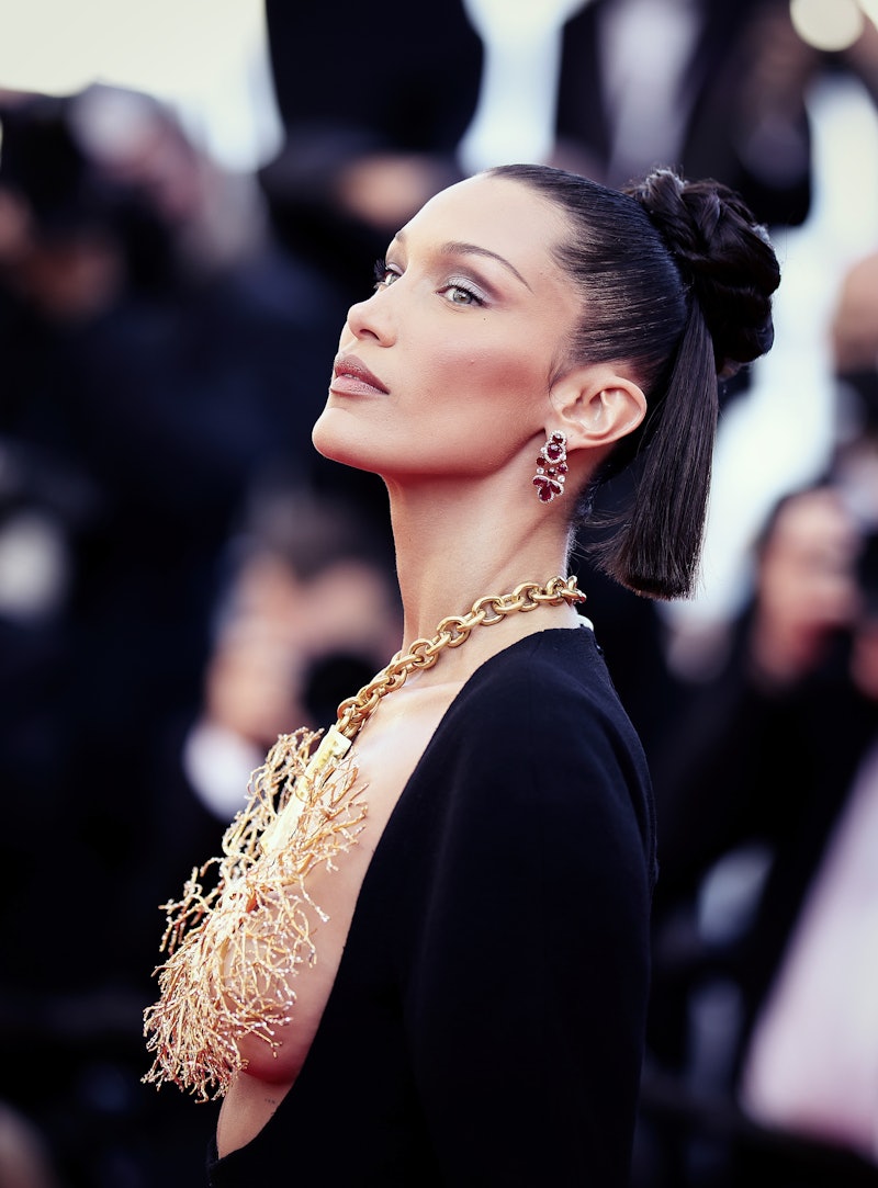 Bella Hadid wearing a black dress and a golden tree shaped necklace that covers her breast, with the...