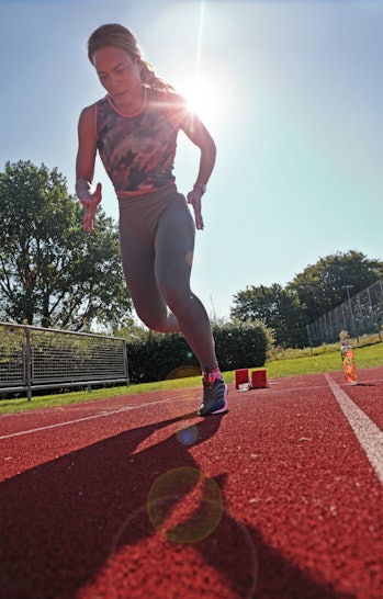 Woman sprinting on running track with sun behind her.
