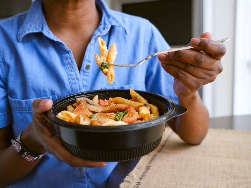 Close-up of woman enjoying takeout pasta and chicken dish