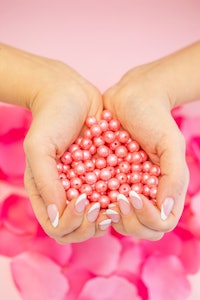 Hands with French nails over Pink Rose Petals creating a handful of Pearls Heart shape