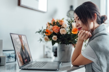 Young Asian woman receiving a flower bouquet while having a video call on laptop with her lover on V...
