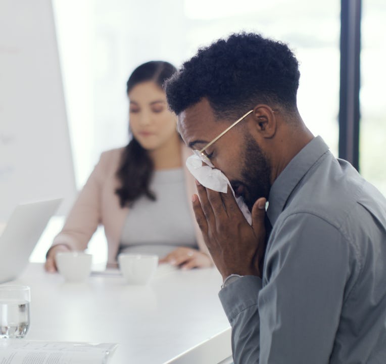 Shot of a businessman blowing his nose while sitting in the boardroom with colleagues