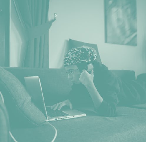 Child watches the screen on his laptop while lying down on a sofa