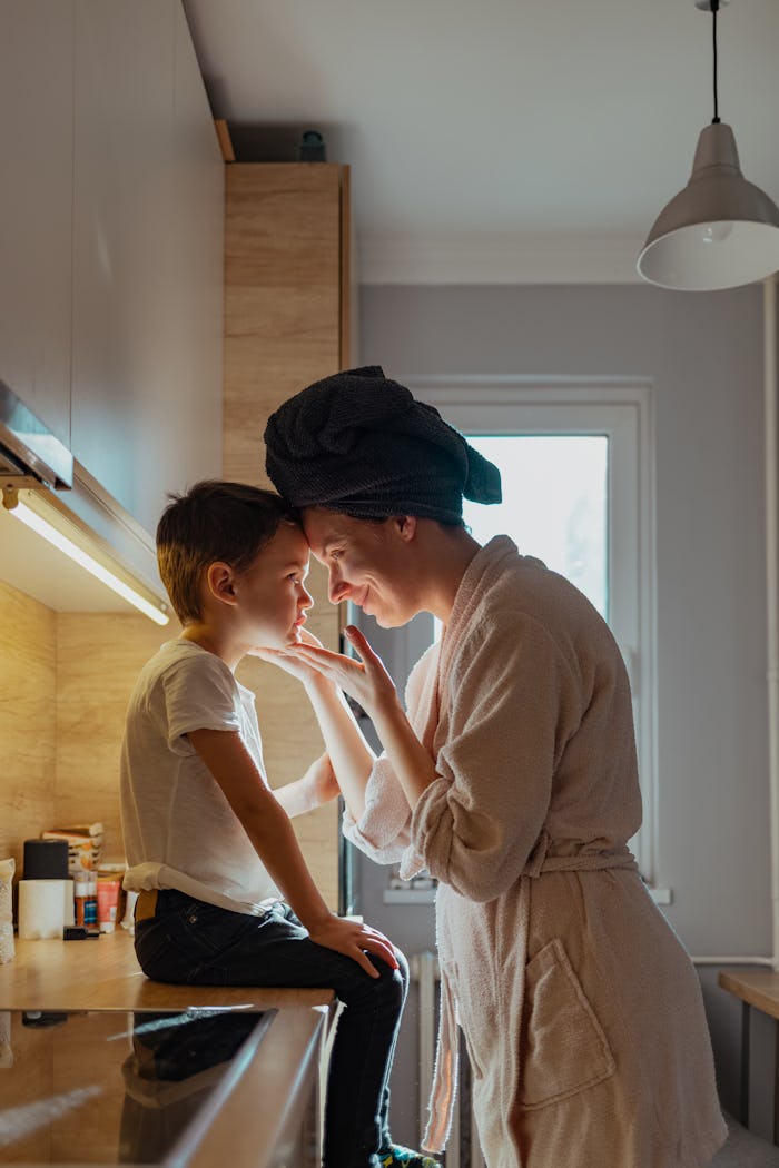 Boy being kissed by his mother while sitting on kitchen counter during the day.