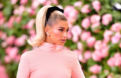 Hailey Bieber wearing a pink turtleneck gown and black hair bow at the Met Gala in 2019.