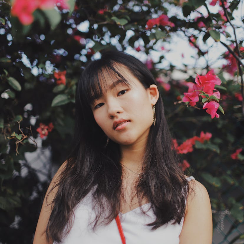 Young woman standing in front of flowers, knowing her unlucky zodiac sign will have the worst week o...